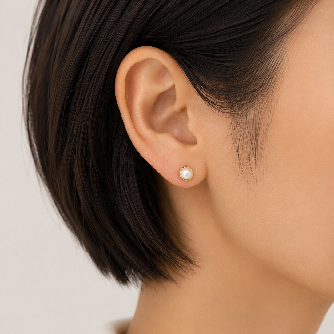 Close-up of an ear wearing a pearl earring with a neutral background